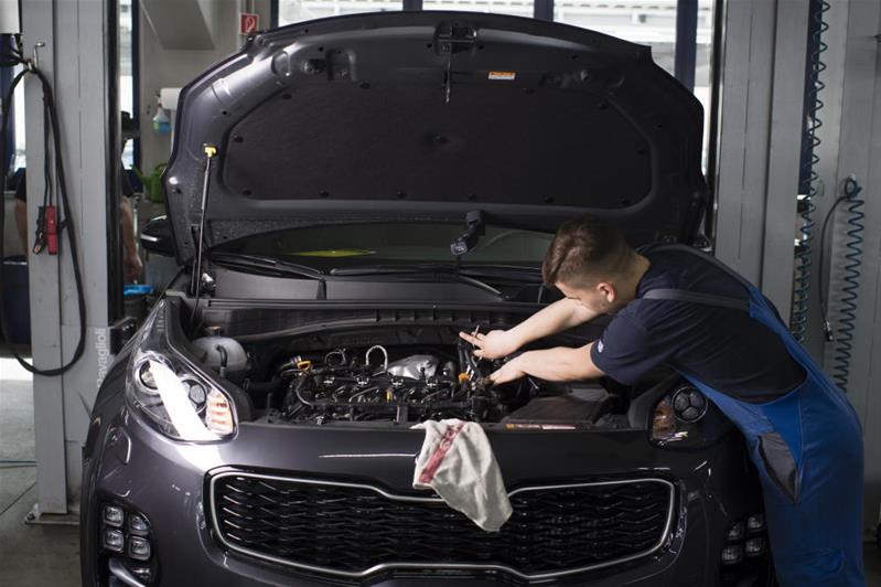 Ein Techniker beugt sich über den Motor eines Autos und repariert Teile.